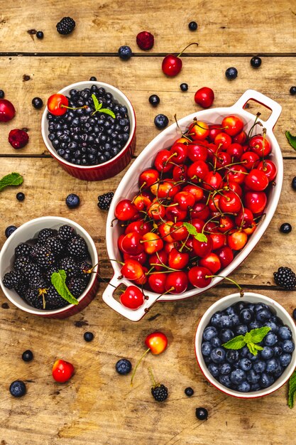 Assorted berries in bowls: bilberry, blueberry, currant, blackberry, cherry and raspberry. Old wooden table background, top view