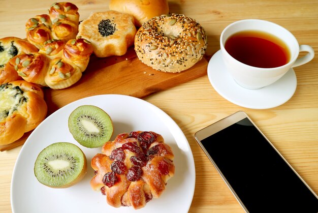 Assorted breads, kiwi fruit and hot tea for breakfast with mobile phone, modern lifestyle concept