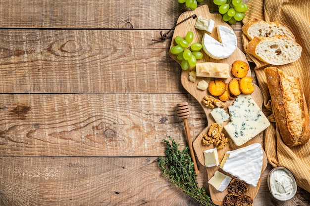 Assorted Cheese Brie, Camembert, Roquefort, parmesan, blue cream cheese with grape, fig, bread and nuts. wooden background. Top view. Copy space.