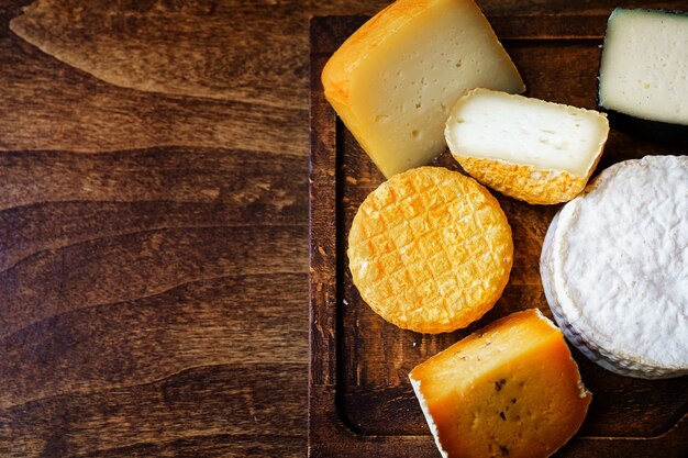 Assorted cheese heads on a cutting board on a wooden table.
cheese factory and cheese shop. natural farm dairy products.
advertising and menus. copy space