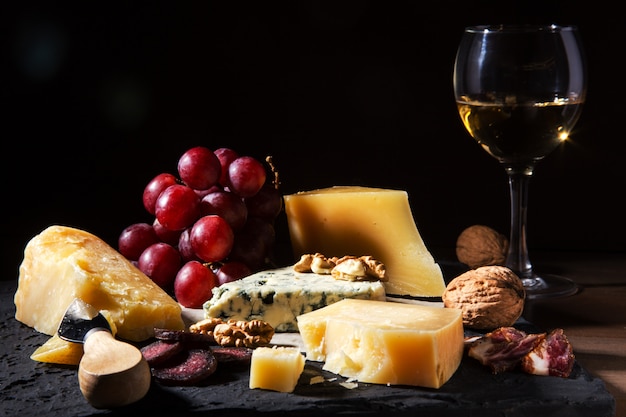 Ассорти сыров, орехов, винограда, фруктов, копченого мяса и бокала вина на сервировочном столе