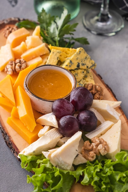 Assorted cheeses  with honey, walnuts and grapes. Tasty cheese plate on a wooden board. Closeup