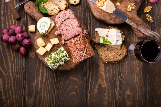 Assorted cheeses on wooden boards plate, grapes, bread wine and pate 