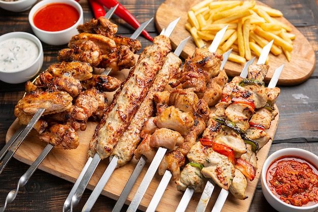 Assorted chicken kebabs with French fries and sauce on dark wooden