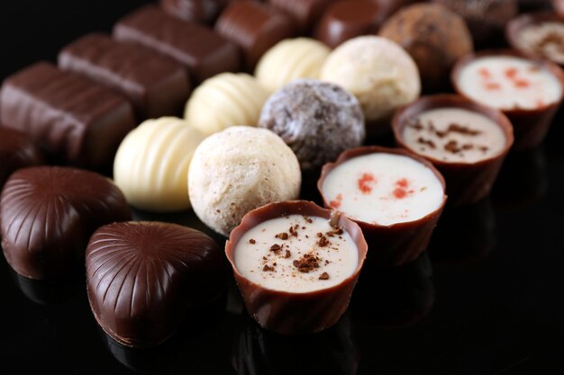 Assorted chocolate candies on black background, close up