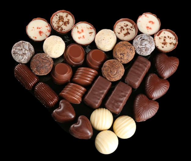 Assorted chocolate candies in form of heart on black background