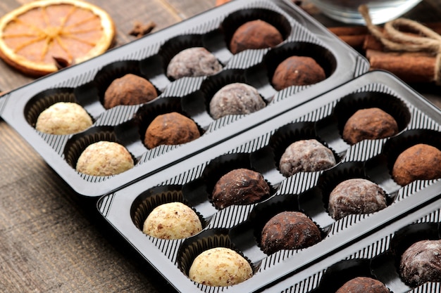 Photo assorted chocolates. candy balls of different types of chocolate in a box on a brown wooden table.