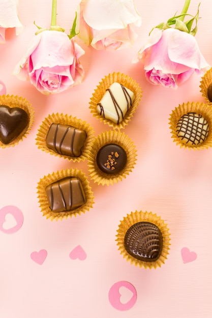 Assorted chocolates with pink roses on pink background.