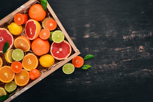 Assorted citrus fruit in a wooden box. Orange, tangerine, grapefruit, lemon. On a wooden background. Top view. Copy space.