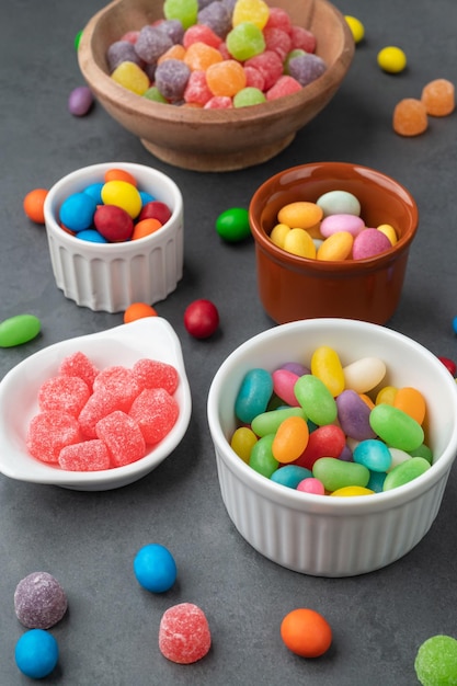 Assorted colorful candies in bowls over stone background