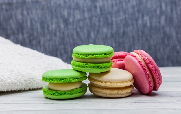 Assorted colorful macaroons on a wooden table and blue background, next to a white towel