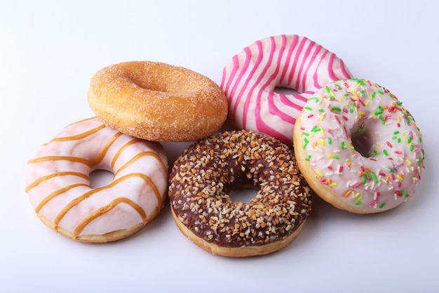 Assorted delicious homemade doughnuts in the glaze, colorful sprinkles and nuts isolated on white background.