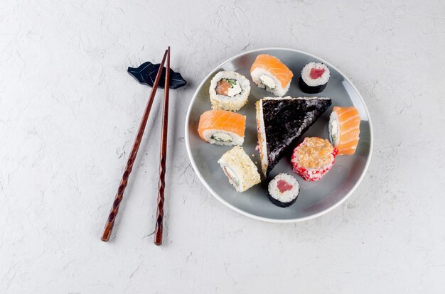 Assorted different sushi rolls on a plate and soy sauce, ginger, wasabi and chopsticks