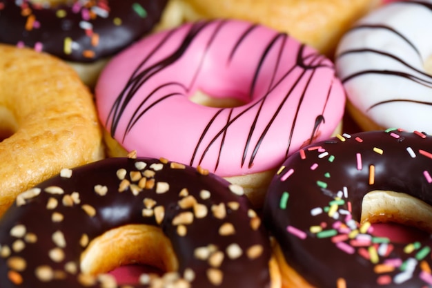 Photo assorted donuts with chocolate frosting topping sprinkles donuts colorful variety and variety of flavors mix of multi colored sweet donuts with frosted sprinkled on pink background top view