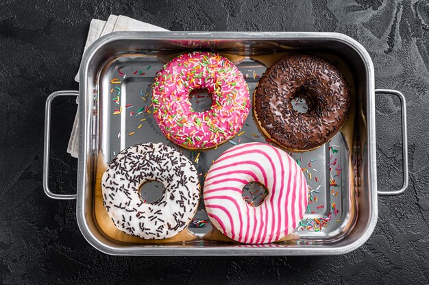 Assorted donuts with chocolate, pink glazed and sprinkles Doughnut. Black background. Top view.