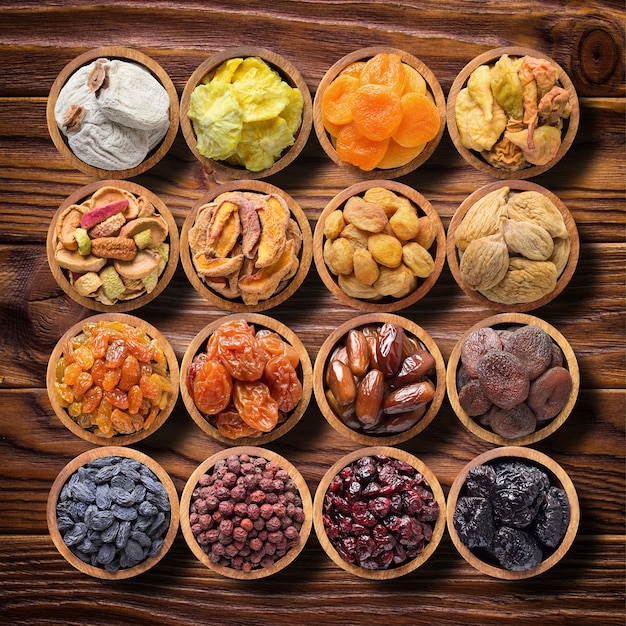 Assorted dried fruits and berries in wooden bowls, top view.