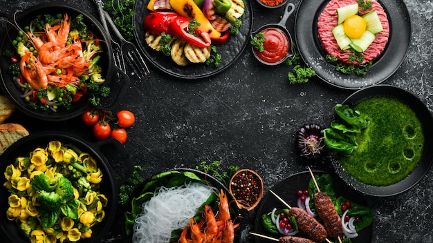 Assorted food and dishes of vegetables, meat and fish on a black stone background. Top view. Free space for your text.