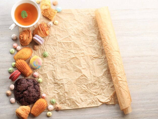 Assorted French Pastry with Copy Space on White Marble Table for text or Recipe. Macaroons, Meringue, Madeleine, Craquelin Eclair, Mini Croissant, Big Chocolate Cookies, and A Cup of Tea