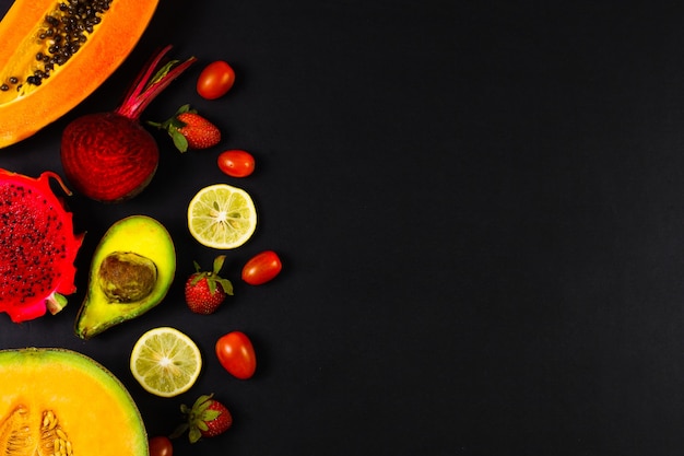 Assorted fresh fruits on black background in creative flat lay composition with copy space