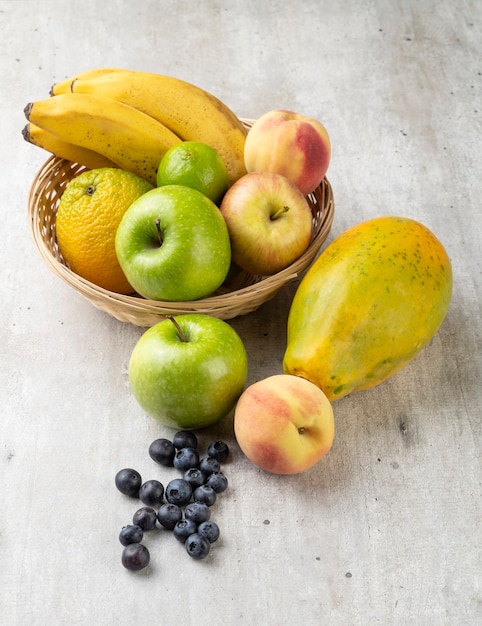 Assorted fruits in a basket over light grey table.