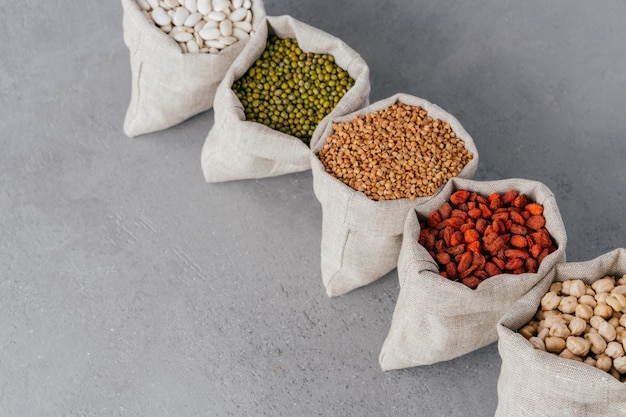 Assorted gluten free grains in linen cloth bags on grey background.