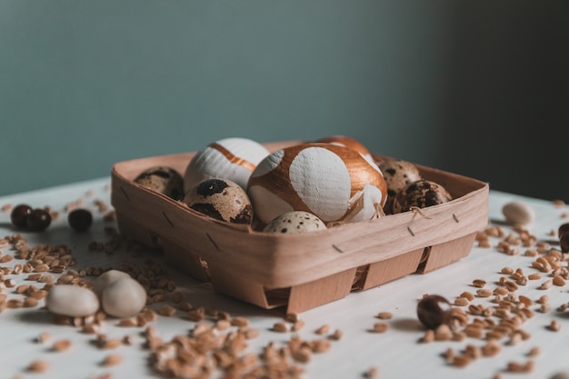 Assorted gold Easter eggs, chocolate dragee candies and millet in a basket on green wall