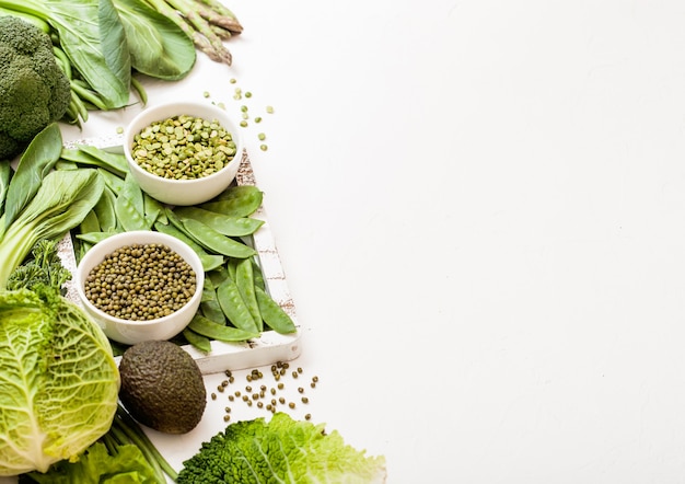 Assorted green toned raw organic vegetables on white surface