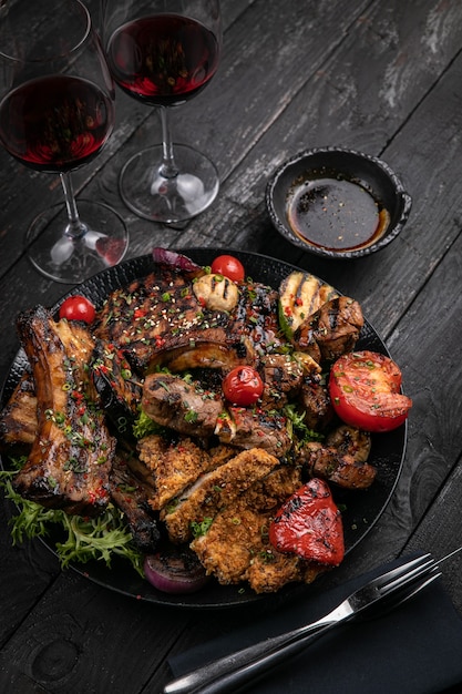 Photo assorted grilled meat with sauce and red wine on a black table