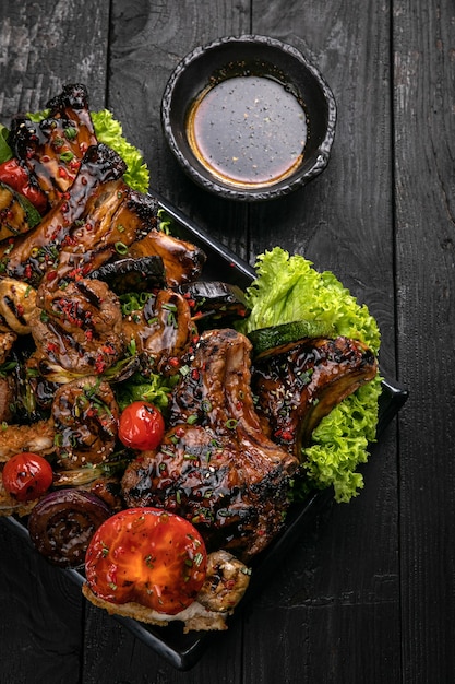 Assorted grilled meat with sauce and red wine on a black table