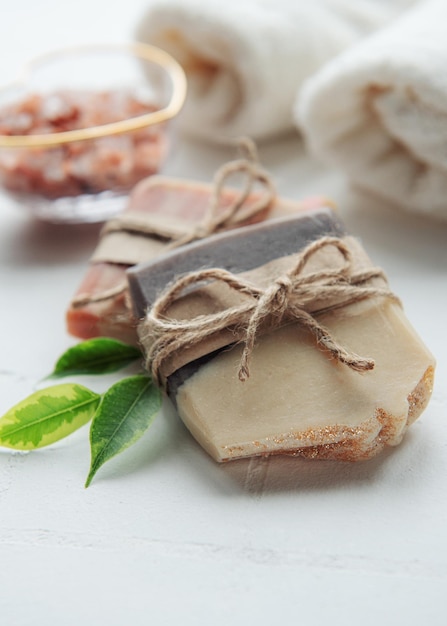 Assorted handmade soap bars and green leaves on white tile background