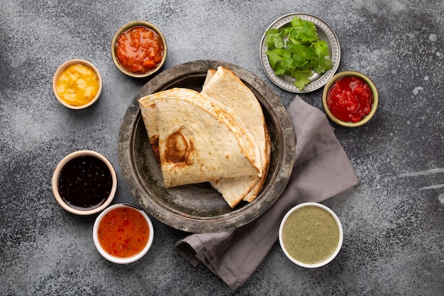 Photo assorted indian chutneys in rustic bowls and flatbread on grey concrete background. top view of flatbread with colorful chutney, traditional indian sauces and dips as a snack or side dish, close-up