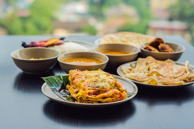 Ассорти из индийских блюд на темном деревянном фоне. Блюда и закуски индийской кухни. Карри, курица в сливочном масле, рис, чечевица, панир, самса, наан, чатни, специи. Миски и тарелки с индийской едой