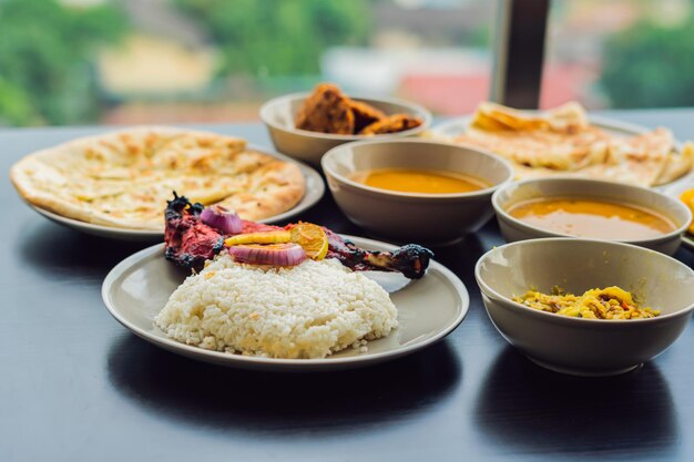 Assorted indian food on dark wooden background. Dishes and appetizers of indian cuisine. Curry, butter chicken, rice, lentils, paneer, samosa, naan, chutney, spices. Bowls and plates with indian food