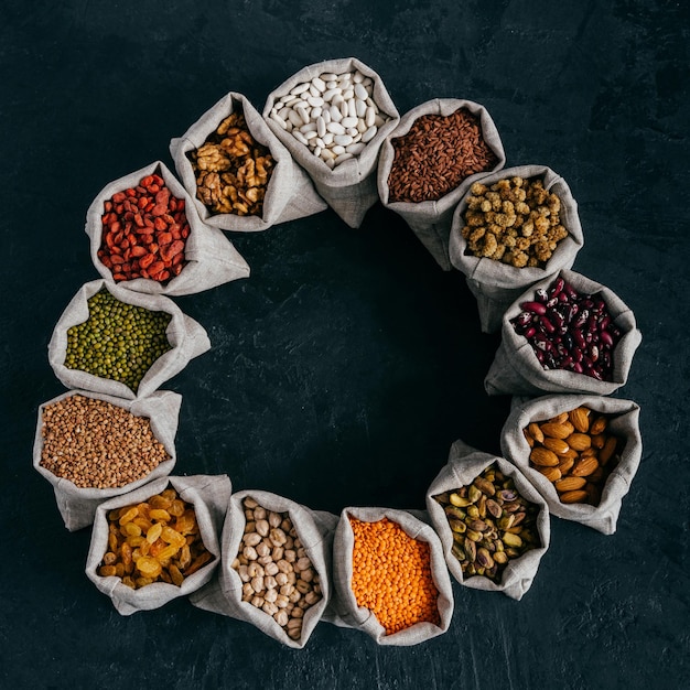 Assorted legumes and beans in sacks standing in circle isolated over dark background with copy space in middle Healthy eating concept