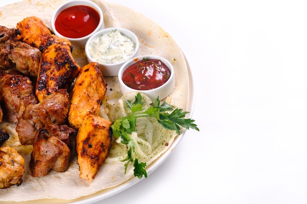 Assorted meat on pita bread with vegetables and sauces on a white plate on a white isolated background.