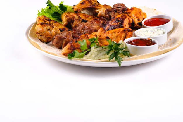 Assorted meat on pita bread with vegetables and sauces on a white plate on a white isolated background.