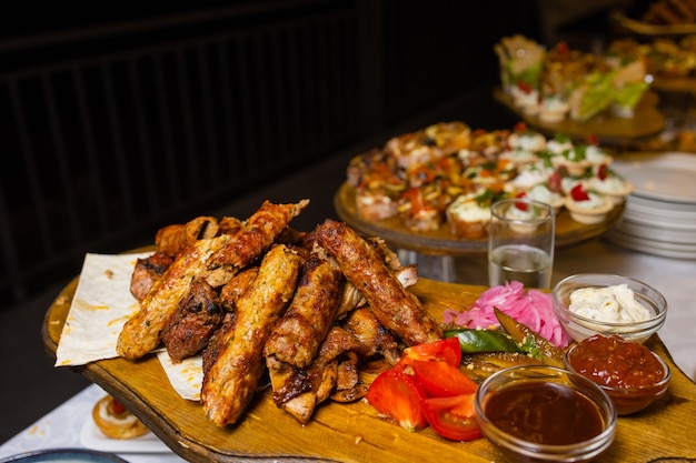 Assorted meat on a plate close up. Different types of meat and potatoes in a heap. Appetizer on a large plate with sauces.