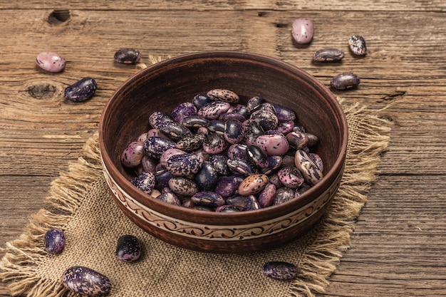 Assorted multicolored beans in a ceramic bowl. Raw healthy ingredient for cooking useful food. Old wooden table, close up