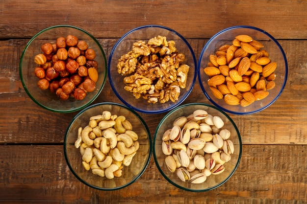 Assorted nuts in a glass bowl on a wooden table. 