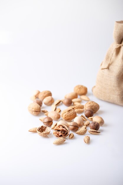 Assorted nuts in the shell on a white background walnuts pecans almonds macadamia Nuts in a burlap bag Selective focus closeup Place for text