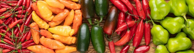 Assorted peppers over wooden table, panoramic format.