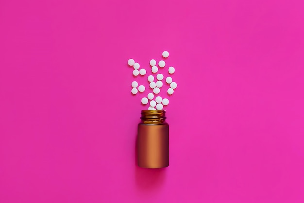 Assorted pharmaceutical medicine pills tablets and capsules and bottle on pink background Copy space for text