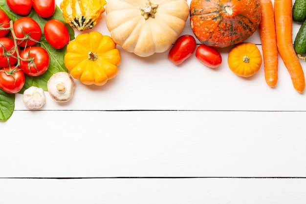 Assorted raw organic fresh vegetables on white wooden table. Fresh garden vegetarian food. Autumn seasonal image of farmer table with mushrooms, rye, cucumbers, tomatoes, eggplant, pumpkins.