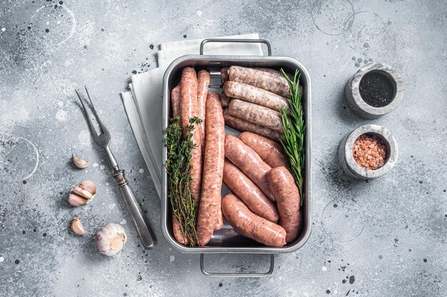 Assorted raw sausages Beef pork lamb and chicken mince meat sausages in a steel kitchen tray with herbs Gray background Top view