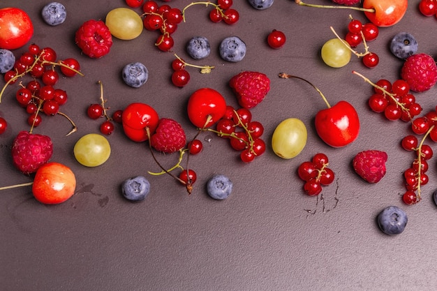 Assorted ripe berries, scattered on a black stone background.\
fresh raspberries, blueberries, grape, sweet cherries, and red\
currants. a modern hard light, dark shadow, top view