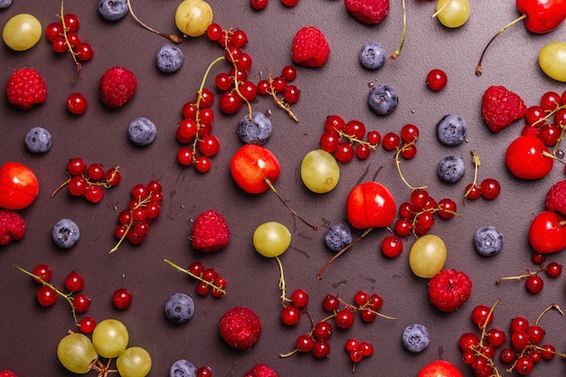 Assorted ripe berries, scattered on a black stone background.\
fresh raspberries, blueberries, grape, sweet cherries, and red\
currants. a modern hard light, dark shadow, top view