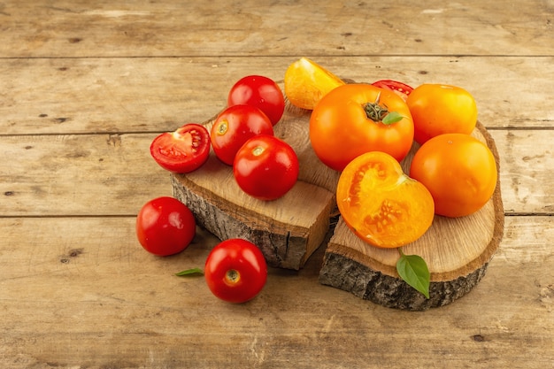 Assorted ripe tomatoes on a wooden stand. Fresh red and orange organic vegetables, basil leaves. Old wooden table, copy space