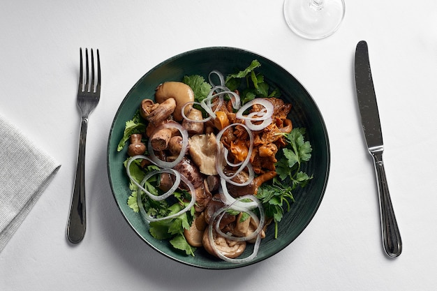 Assorted salted mushrooms, on a teatka, a mix of boletus mushrooms, chanterelles, oyster mushrooms on a plate with onions and herbs top view.