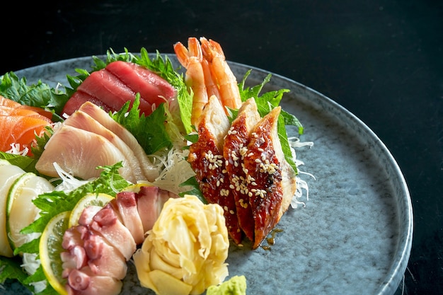 연어, 새우, 참치, 문어, 가리비, 장어의 모듬 사시미. 고전적인 일본 요리. 음식 배달. 블랙에 절연