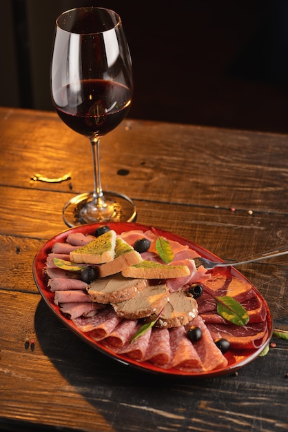 Assorted sausages, jamon and ham with slices of fried bread on a red plate. On a wooden table